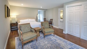 Une chambre à coucher avec un lit, deux fauteuils, une table de chevet, une lampe et une porte.