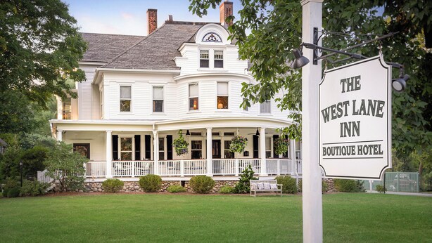 En stor, hvid bygning med to etager, buet veranda og et skilt, der siger "The West Lane Inn Boutique Hotel".