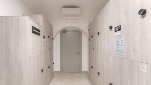 Pasillo de hotel con taquillas numeradas 11 y 12, un equipo de aire acondicionado y una puerta al final.