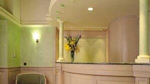 Un área de recepción con un mostrador curvo, una silla y un florero con flores.