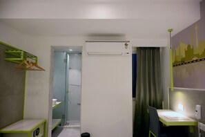 A hotel room with a bed, bedside table, and a desk with a chair. There is a window with curtains, a wall-mounted air conditioner, and a wall with a cityscape mural. - Sun City (New Delhi)