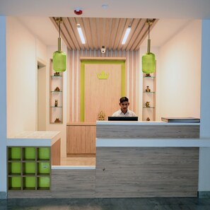 A reception desk with a wooden finish, a crown-shaped decoration on the wall, and shelves with decorative items. - Sun City (New Delhi)