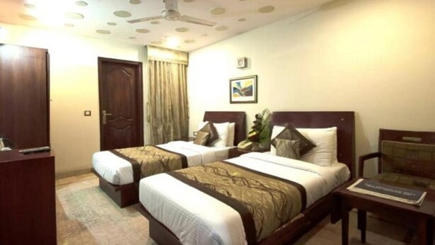 A hotel room with two beds, a desk, a chair, and a ceiling fan. - Sun City (New Delhi)