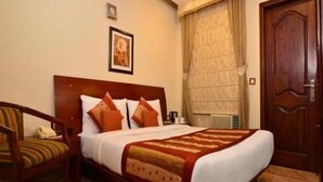 A hotel room with a wooden bed, a chair, a framed picture on the wall, and a door. - Sun City (New Delhi)