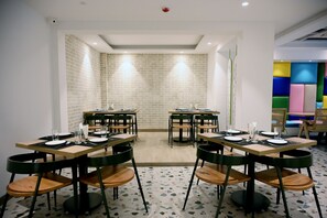 Un espace repas comprenant plusieurs tables et chaises, un mur en briques et une décoration murale colorée.