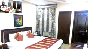 A hotel room with a large bed, a bedside table, a nightstand, a framed picture on the wall, and a window with curtains. - Sun City (New Delhi)