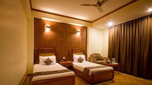 A hotel room with two wooden beds, a nightstand, a chair, a ceiling fan, and a large window with curtains. - Sunstar Grand (New Delhi)