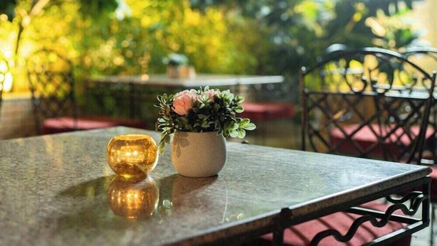 A table with a reflective glass top, a potted plant with pink flowers, and a glass object. - Sunstar Grand (New Delhi)