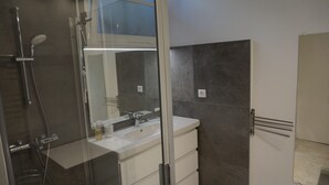 Un baño moderno con cabina de ducha de vidrio, lavamanos blanco y un espejo grande.
