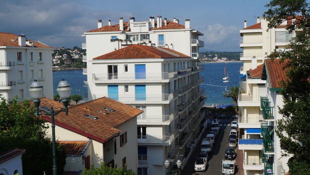Un edificio costero con varios balcones, vista al mar y coches aparcados en la calle.