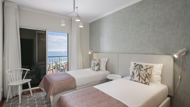 A hotel room with two beds, a balcony with a view, a white chair, and a modern chandelier. - By the sea, Reis Magos IV (Caniço)