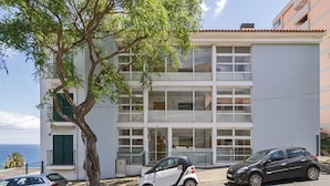 A two-story building with a white facade and balconies. There are three cars parked in front. - By the sea, Reis Magos IV (Caniço)