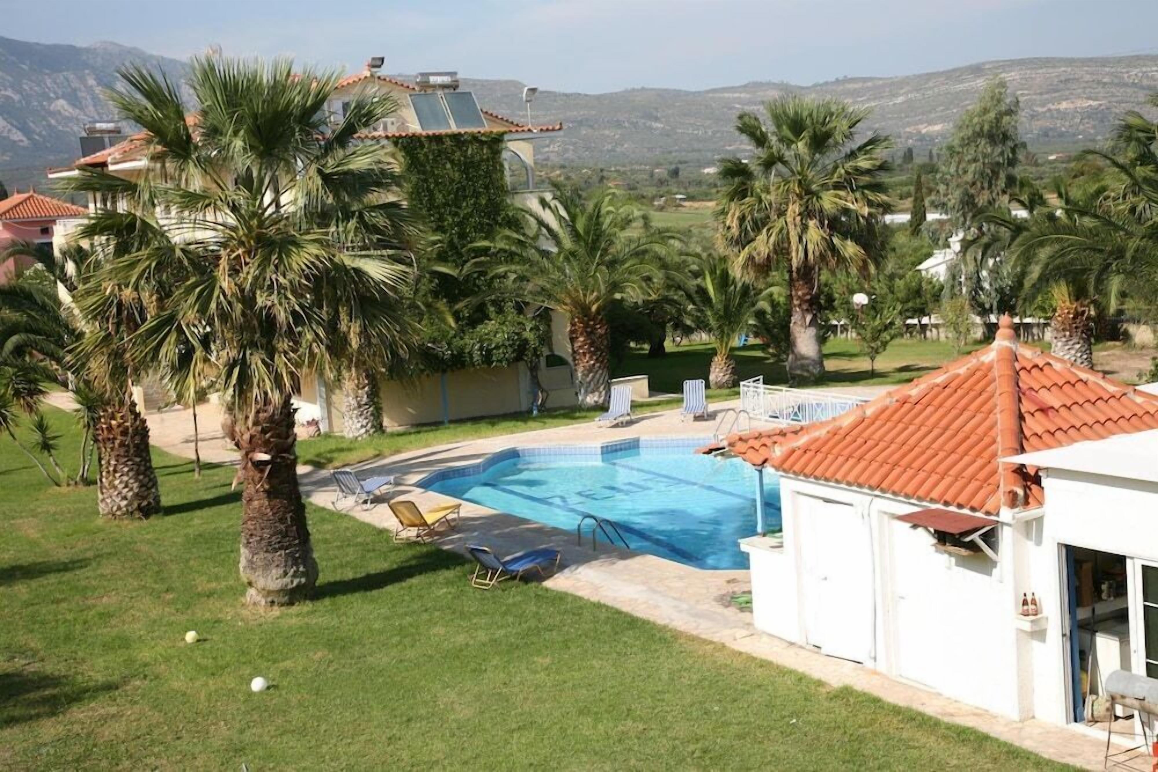 Una propiedad residencial con piscina, palmeras y vistas a montañas distantes.