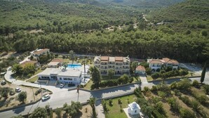 An aerial view of a residential area with multiple buildings, a swimming pool, and a small white structure. - Zeus (Samos)