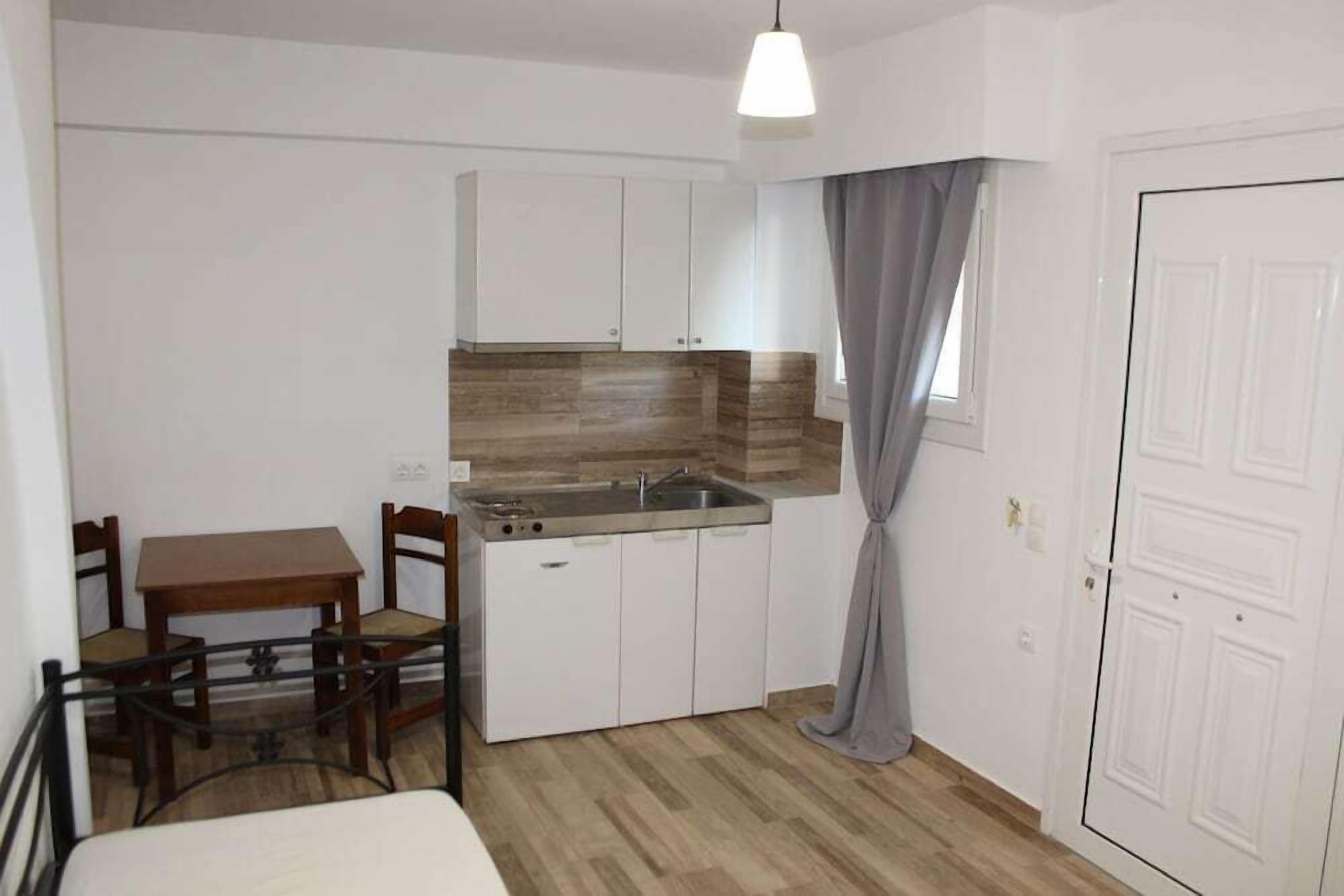 Een compacte keuken met witte kastjes, een houten aanrecht, een spoelbak en een eettafel met stoelen.