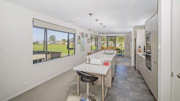 A modern kitchen with a large window, a dining area, and a view of the outdoors. - Pauanui Hangar Retreat - Pauanui Holiday Home (Pauanui)