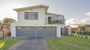 A modern two-story house with a garage, a balcony, and a well-maintained lawn. - Pauanui Hangar Retreat - Pauanui Holiday Home (Pauanui)