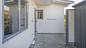 A modern exterior with a glass door leading to a covered outdoor area, a small window, and a metal gate. - Pauanui Hangar Retreat - Pauanui Holiday Home (Pauanui)