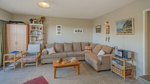 Una sala de estar con sofá, sillones, una mesa de centro, estantería y televisor montado en la pared.