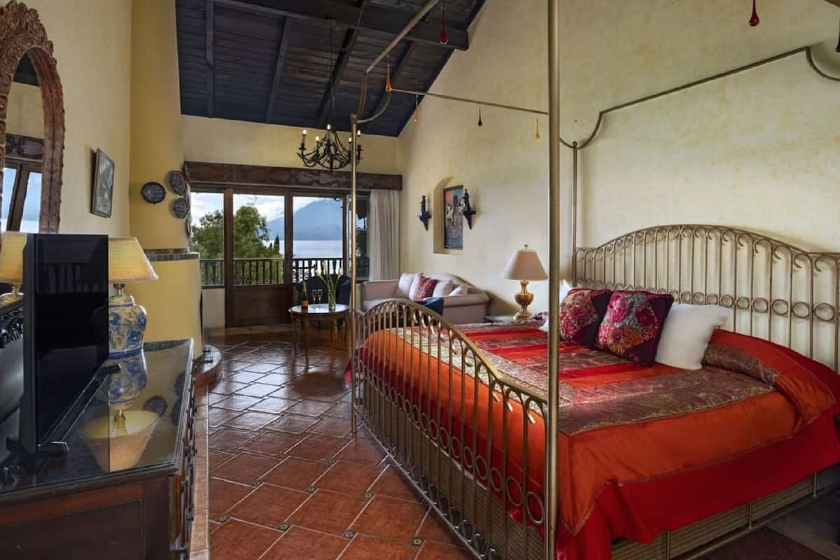 A room with a bed, a TV, a balcony with a view, and a chandelier.