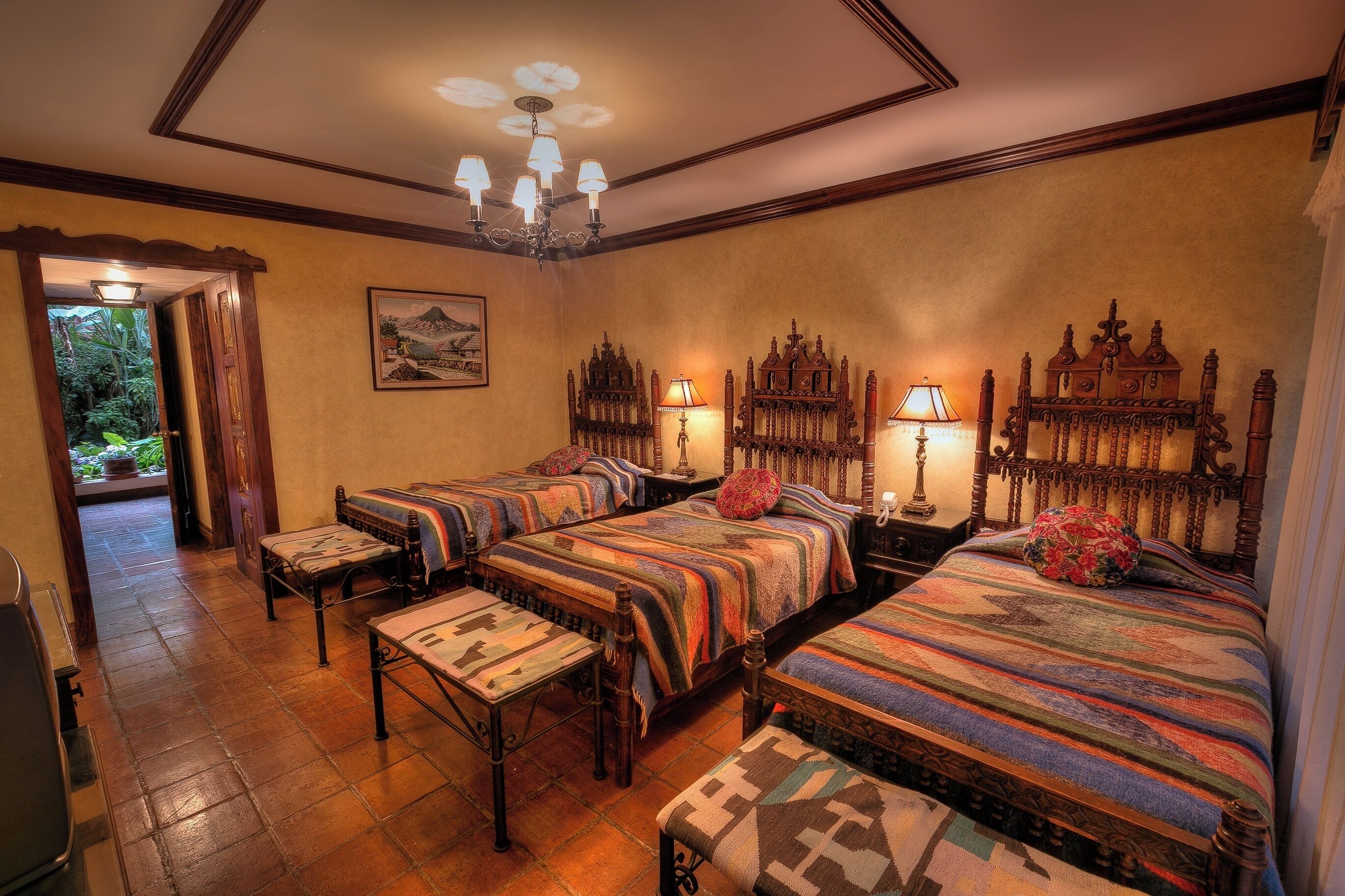 Habitación de hotel con cuatro camas, un candelabro y un cuadro en la pared.