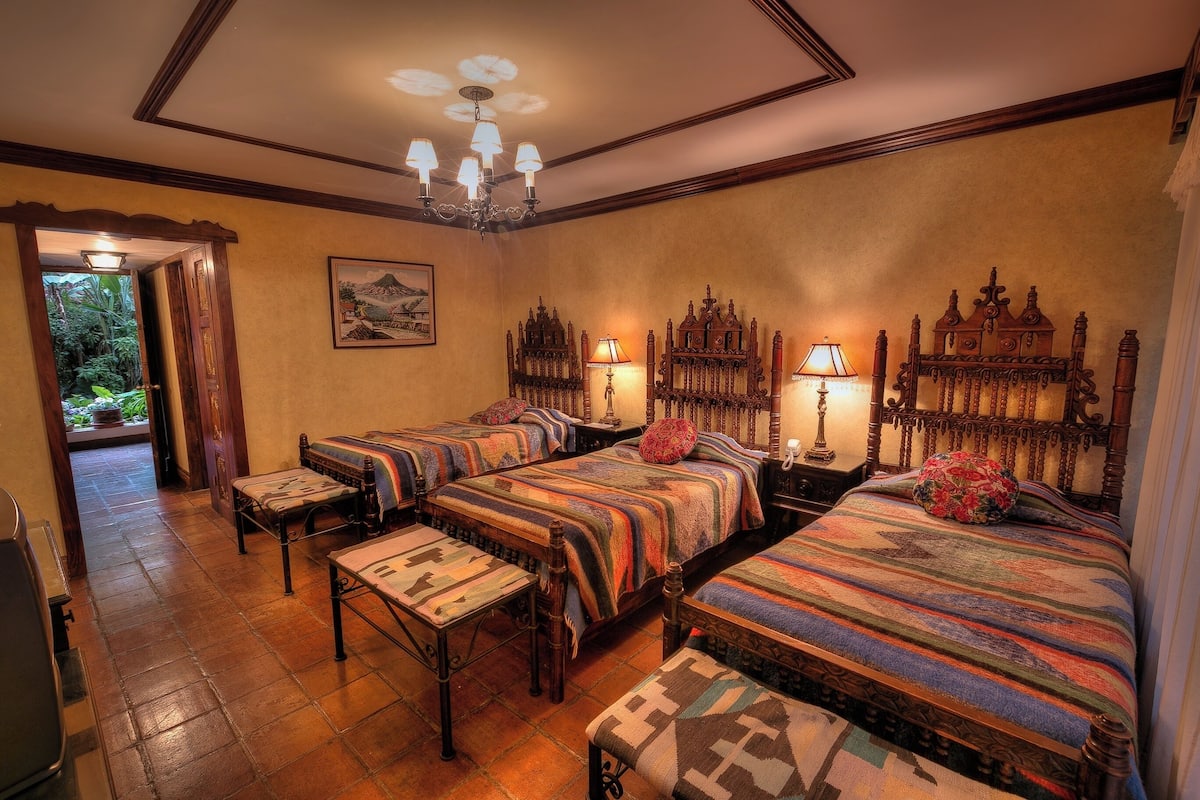 A hotel room with four beds, a chandelier, and a painting on the wall.