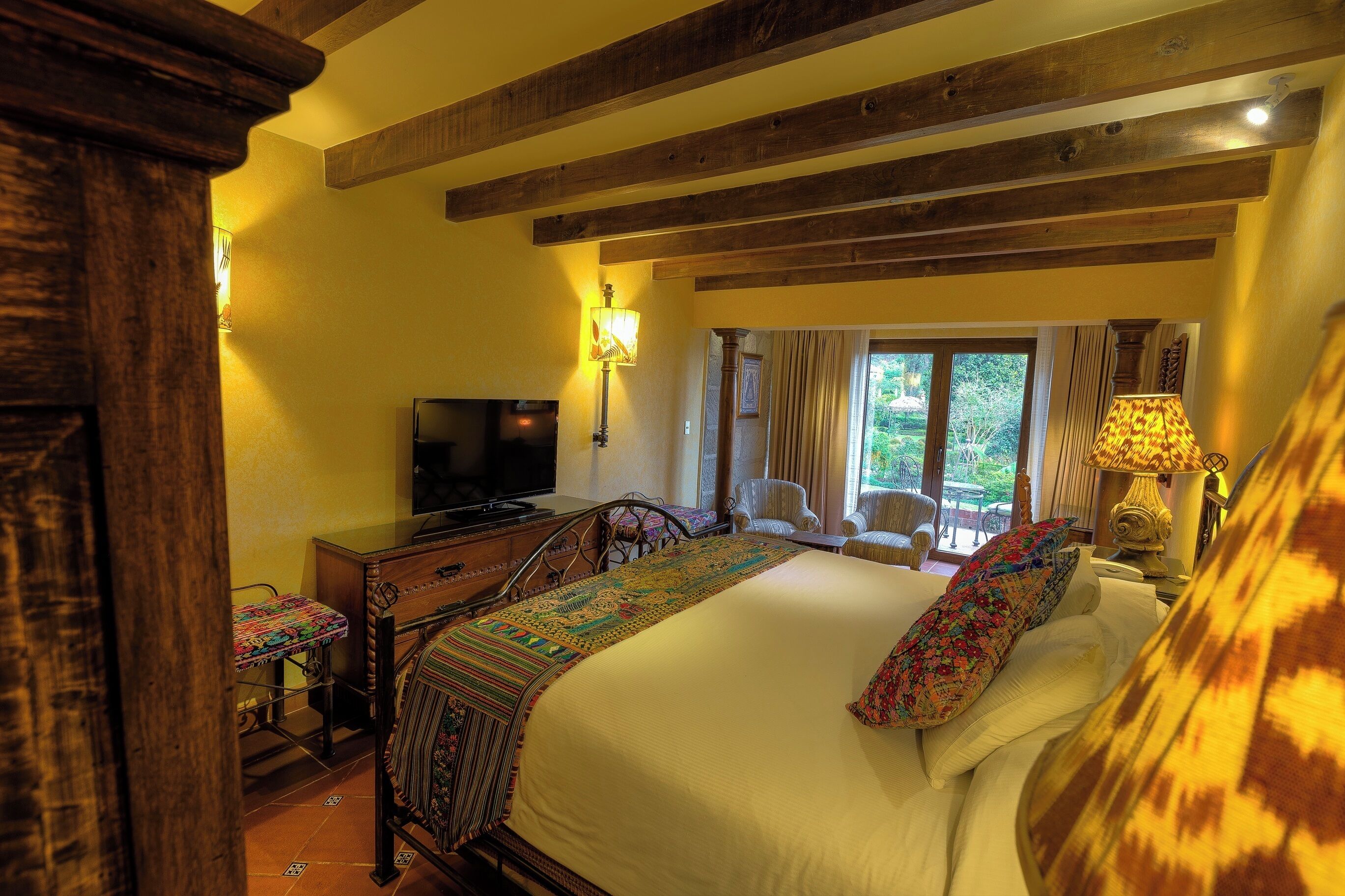 Un dormitorio con cama, televisión, vigas de madera y una ventana con cortinas.