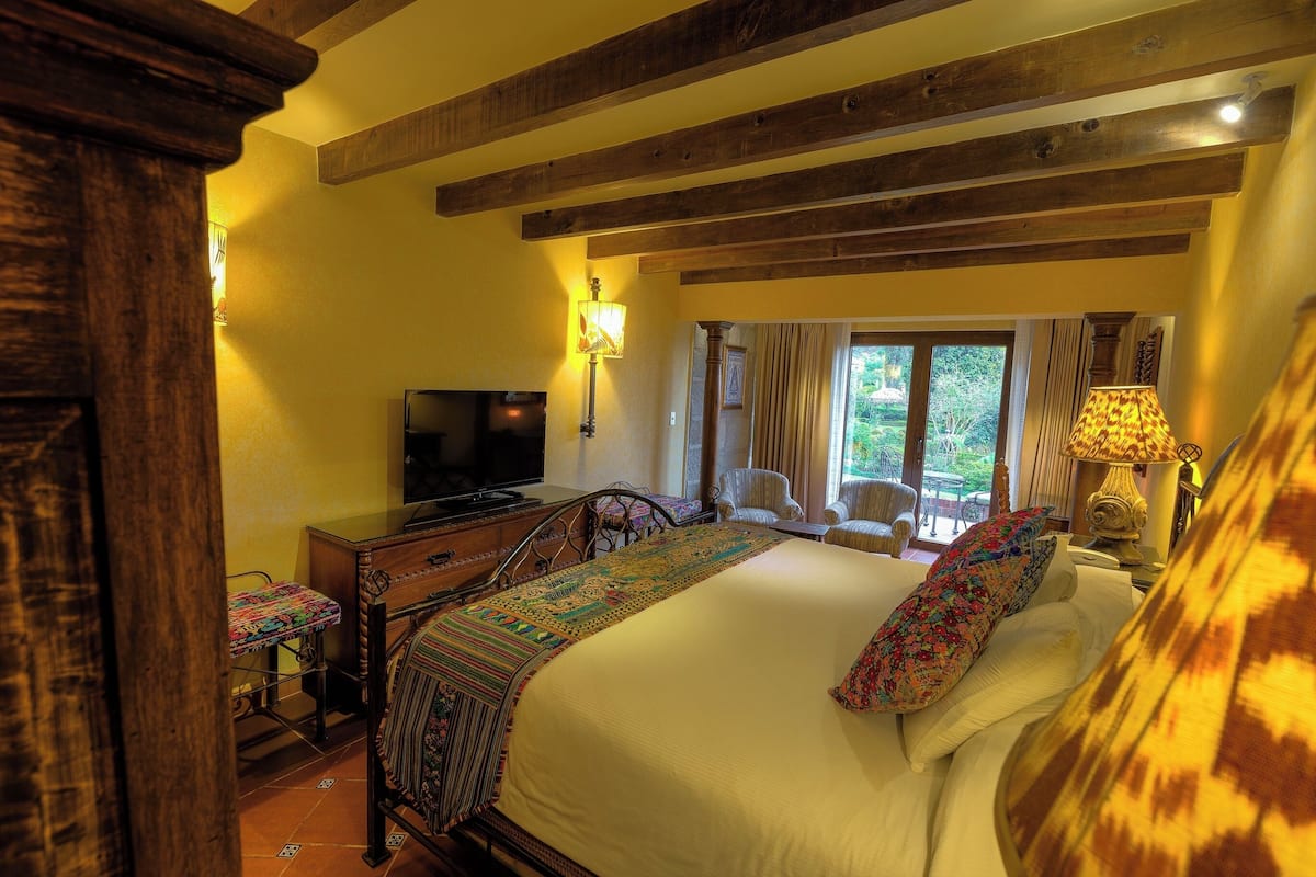 A bedroom with a bed, television, wooden beams, and a window with curtains.