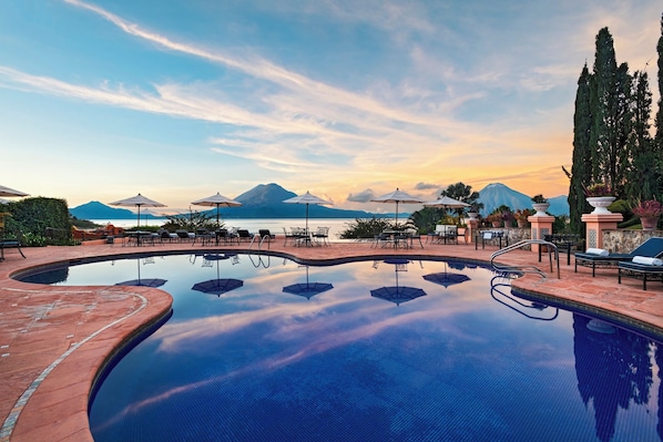 A pool with lounge chairs and umbrellas, surrounded by a landscaped area with a mountain view. - Atitlan (Sololá)