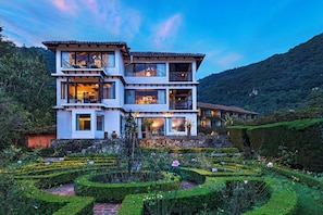 A multi-story building with balconies, surrounded by a well-maintained garden with various plants and flowers. - Atitlan (Sololá)