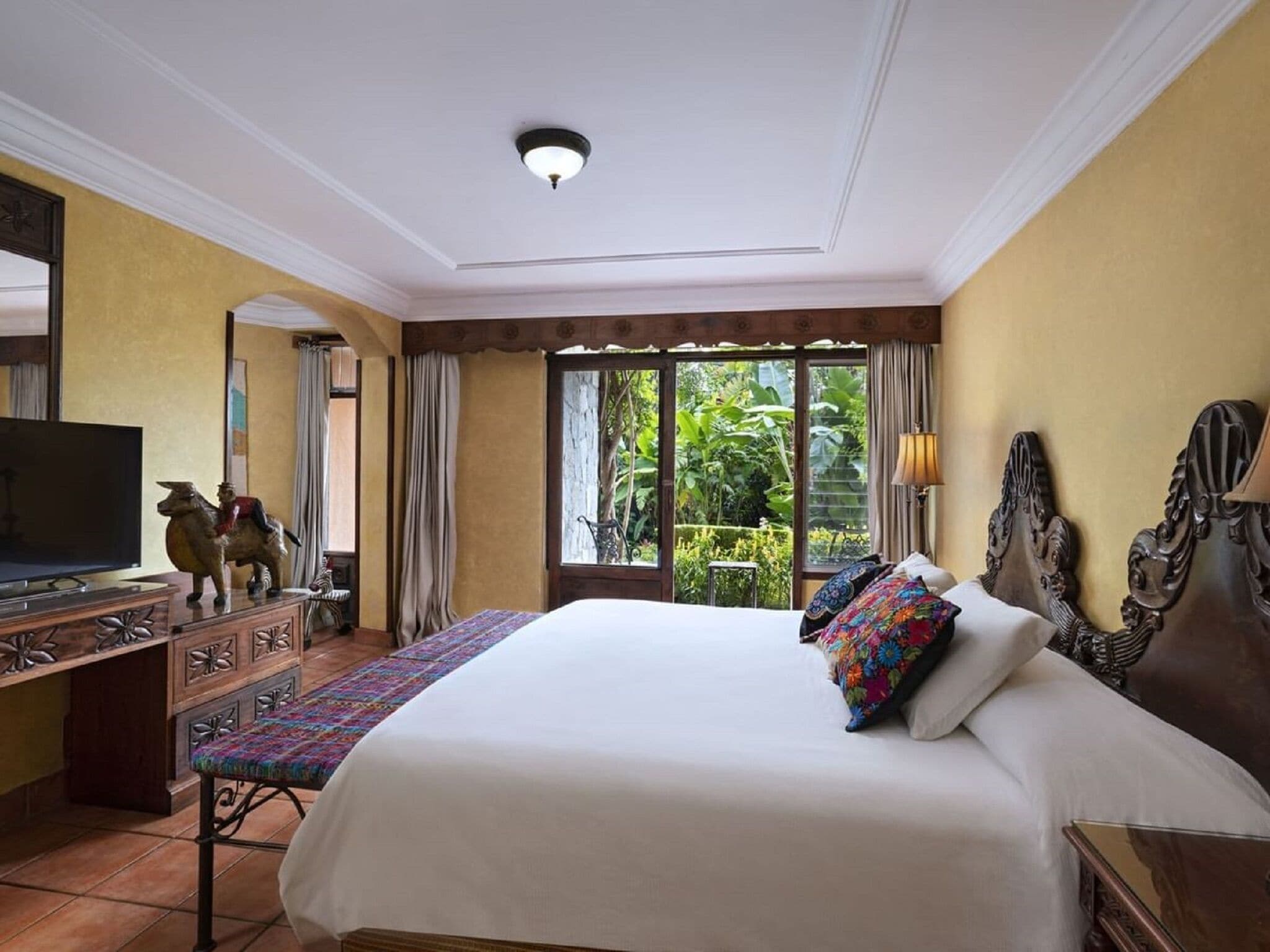 Habitación de hotel con una cama grande, televisión, escritorio con cajones y vistas a zonas verdes.