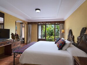 Habitación de hotel con una cama grande, televisión, escritorio con cajones y vistas a zonas verdes.