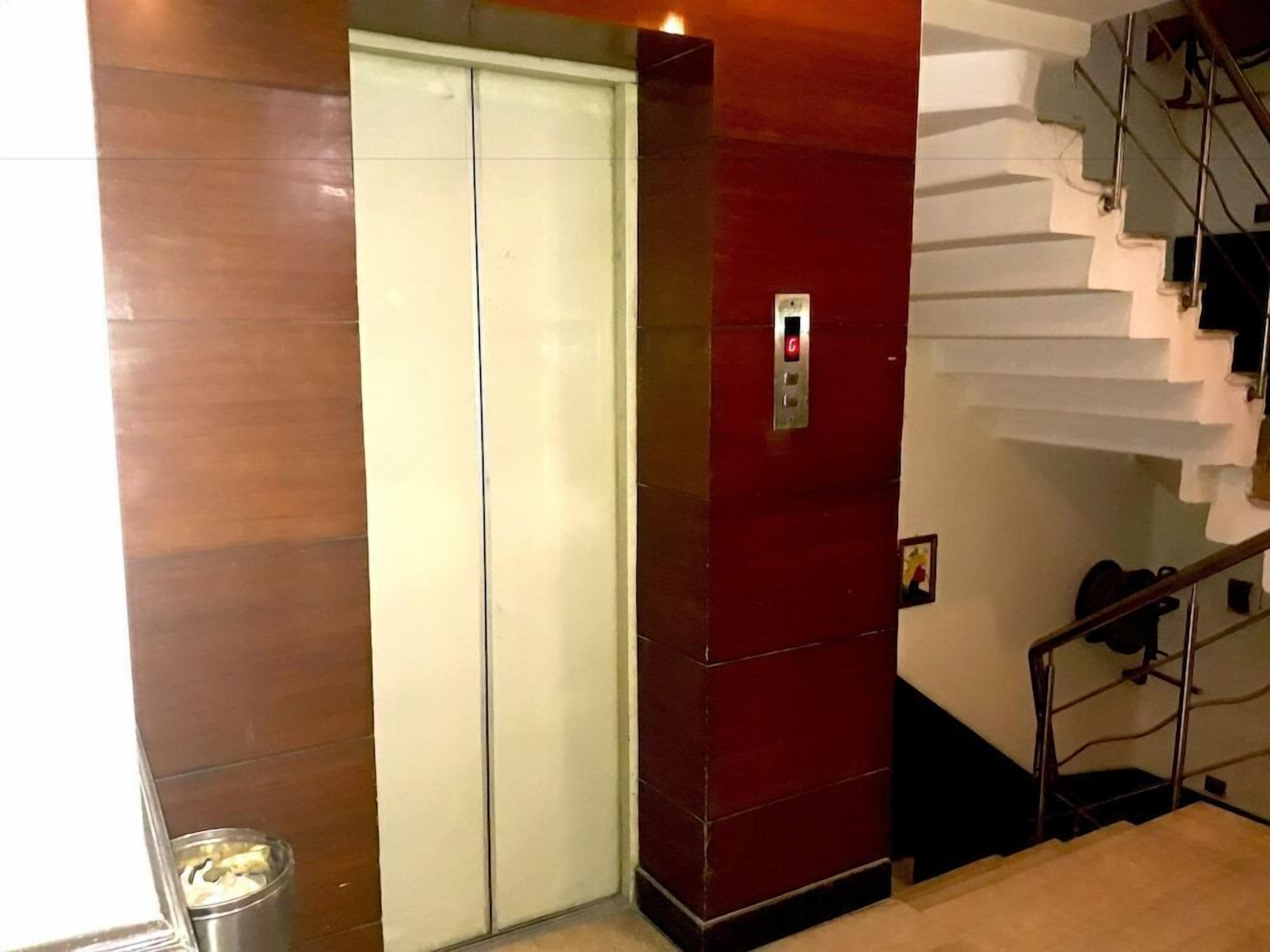 An elevator with a red wall and a white door, next to a staircase with a metal railing.