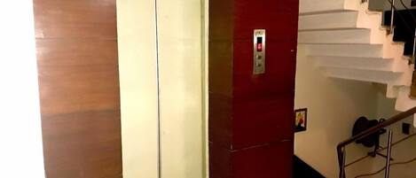 An elevator with a red wall and a white door, next to a staircase with a metal railing.