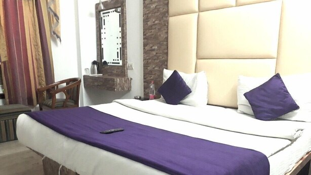 Una cama con un edredón morado, almohadas blancas y un control remoto.