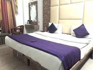 A bed with a purple blanket, white pillows, and a remote control on it. - Karat 87 (New Delhi)