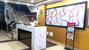 Un mostrador de recepción con encimera de mármol, una escalera al fondo y una gran obra de arte abstracta en la pared.