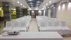 Un salón de conferencias con filas de sillas blancas, un proyector sobre una mesa y una escalera al fondo.