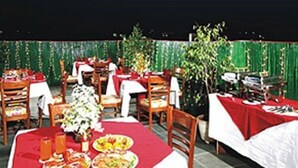 Un área de comedor al aire libre con mesas dispuestas para comidas, rodeada de sillas y follaje.