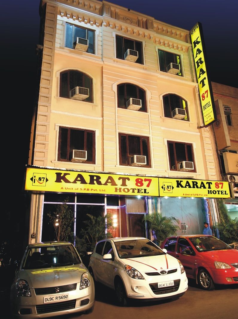 A building with multiple windows and balconies, labeled as "Karat 87 Hotel". There are three cars parked in front.