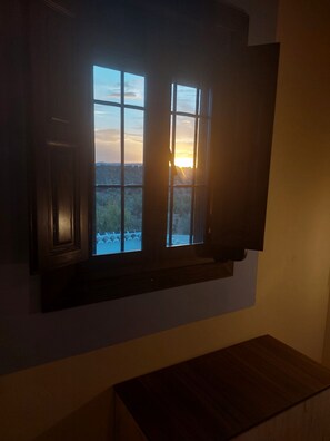 A room with a large window overlooking a landscape, a wooden bench, and a wall-mounted TV.