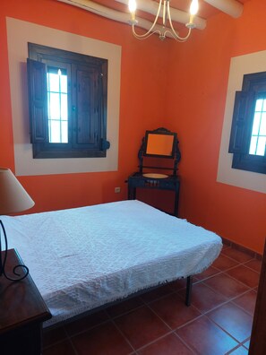A room with a bed, a chair, a table, and a window with a view.