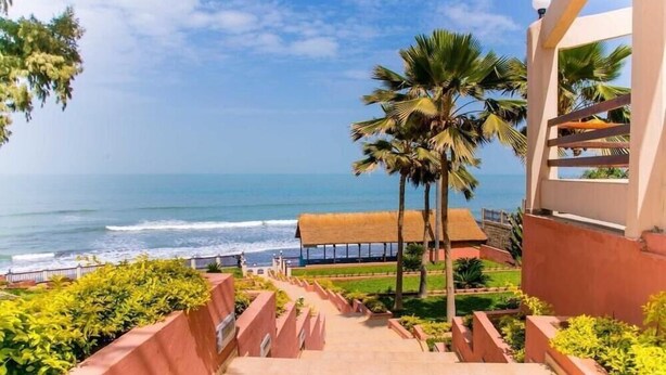 A staircase leading to a beach with palm trees and a clear view of the ocean. - Tropic Gardens Hotel (Bakau)