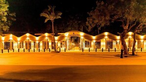 A Tropic Garden Hotel with a series of connected structures, each with a glass facade and illuminated by warm lighting. - Tropic Gardens Hotel (Bakau)