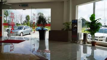 A hotel reception area with a glass door leading outside, a reception desk, and a potted plant.