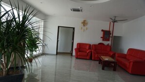 A spacious living room with a large potted plant, two red sofas, a wooden coffee table, and a ceiling fan. - HOTEL KRISTAL SERI ISKANDAR (Bota)