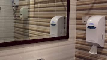A bathroom with a striped tile wall, a mirror, a sink, and a hand sanitizer dispenser.