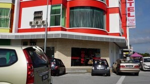 A hotel with a red and white facade, multiple cars parked in front, and a clear sky. - HOTEL KRISTAL SERI ISKANDAR (Bota)