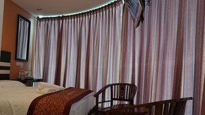 A hotel room with a bed, a wooden chair, a nightstand, and a window with curtains. - HOTEL KRISTAL SERI ISKANDAR (Bota)