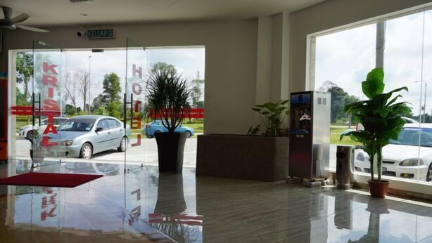 A reception area with a glass door leading outside, a reception desk, a potted plant, and a small office. - HOTEL KRISTAL SERI ISKANDAR (Bota)